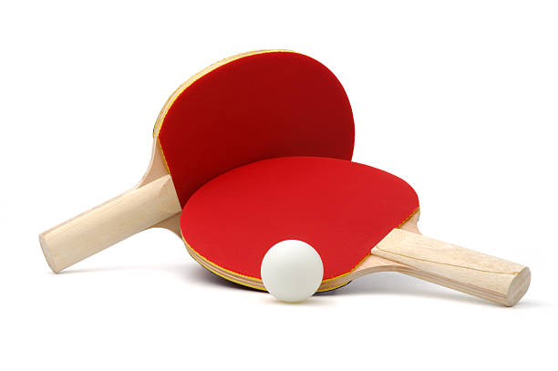 Two red ping pong paddles and a white ping pong ball are arranged on a white surface, with one paddle resting on top of the other.