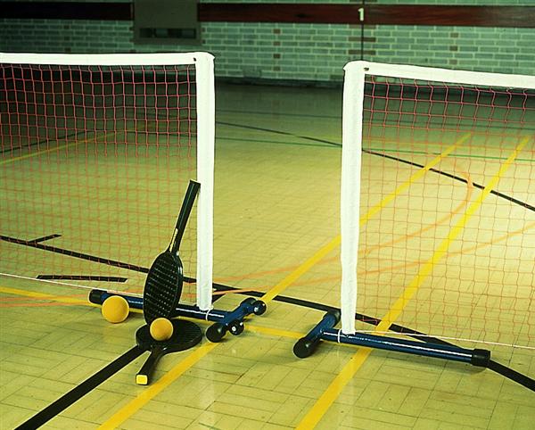 Two mini badminton nets with red mesh stand on an indoor court. Three rackets and three yellow shuttlecocks are placed on the floor in front of the nets.