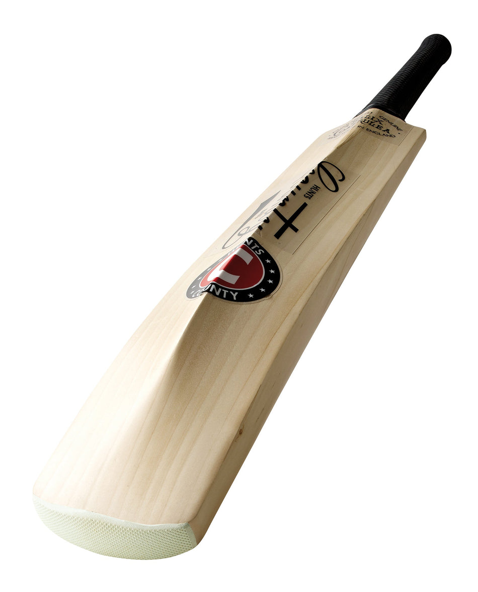 A close-up of the Hunts County Caerulex Senior Cricket Bat, featuring a Grade 1 English Willow blade, black handle, protective toe guard, branded Hunts County sticker, and autograph, shown in its classic shape against a white background.