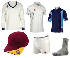 A collection of cricket clothing and gear including two white shirts, a blue shirt, a maroon cap with yellow trim, white shorts, and a grey sock with a logo.