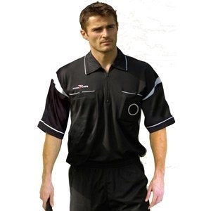 A man wearing a black short-sleeve referee shirt with white accents stands against a plain background, holding something in his right hand, and looking slightly to his left.