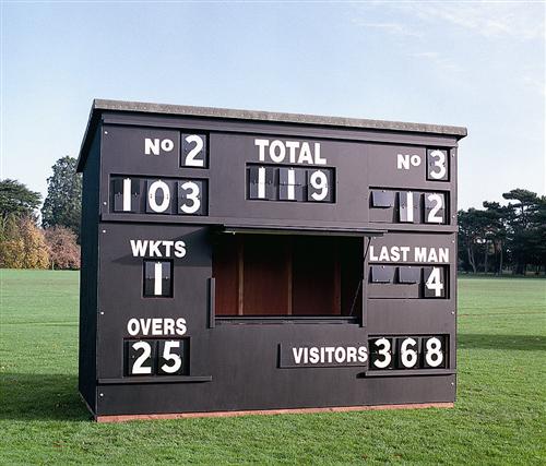A black cricket scoreboard on a grassy field displays scores: Home 119/1 in 25 overs, with 1 wicket lost, last man 4, and visitors 368. Trees and blue sky are in the background.