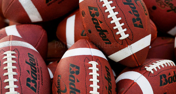 A close-up view of several brown American footballs with white stripes and laces, featuring the brand name Baden printed in black on each ball.