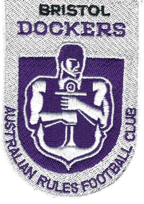 Embroidered patch featuring a muscular figure holding an anchor, with BRISTOL DOCKERS above and AUSTRALIAN RULES FOOTBALL CLUB around a purple and white shield.