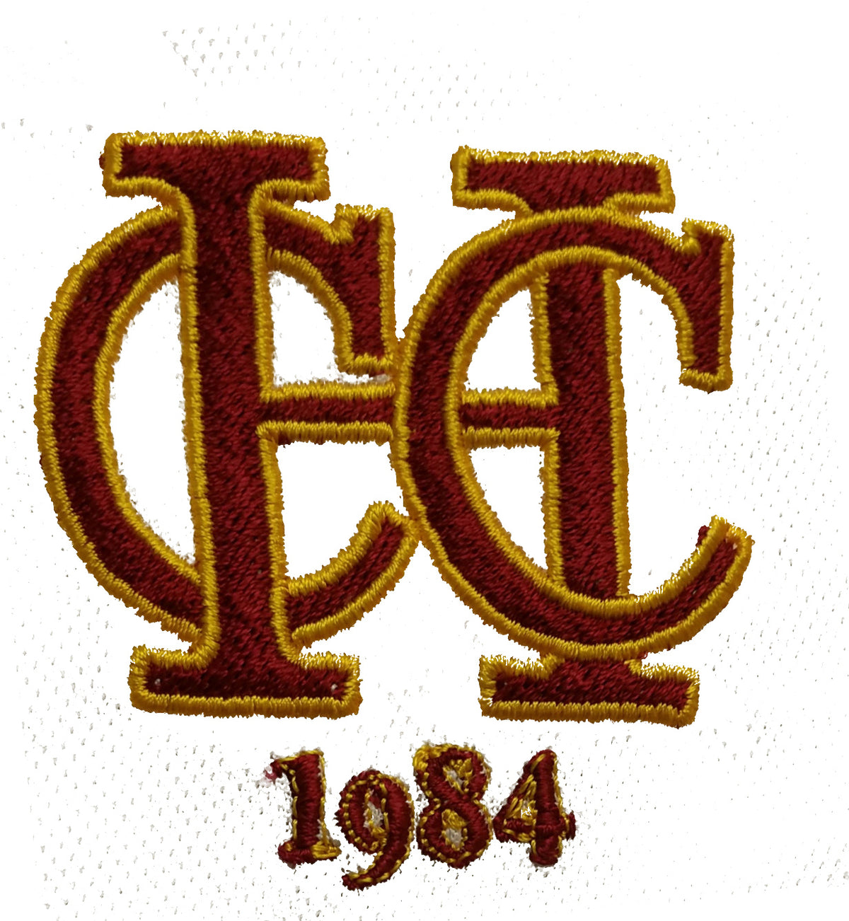 Embroidered maroon and gold overlapping letters C and H with the year 1984 stitched below on a white background.
