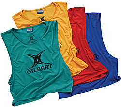 Four sleeveless sports training bibs in green, yellow, red, and blue, each with the Gilbert brand logo printed on the front. The bibs are arranged overlapping each other.