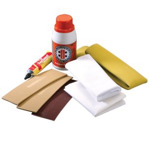 A bicycle tire repair kit with rubber patches, a tube of glue, sandpaper pieces, a small bottle, white cloths, and a yellow tire lever, all arranged on a white surface.