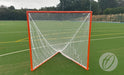 A Harrod Sport Freestanding Competition Lacrosse Goal, featuring a red frame and white netting, stands on green artificial turf marked with white and yellow lines, surrounded by trees in the background—ideal for regulation play.