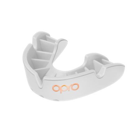 The OPRO Bronze Self Fit Mouthguard is a white, ergonomically designed gum shield with grooves and ridges for optimal teeth protection. It features the Opro brand name in orange on the front, ideal for sports use.
