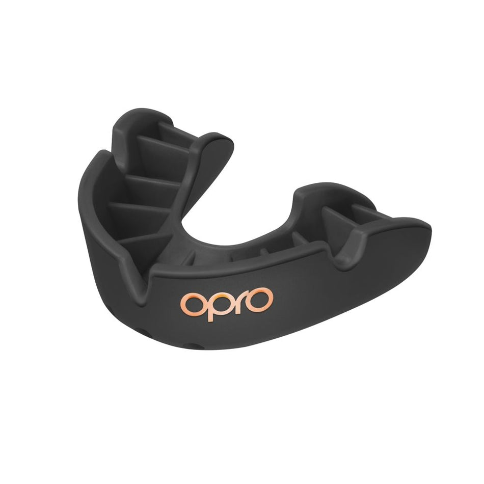 The OPRO Bronze Self Fit Mouthguard by Opro is a black, contoured mouthguard featuring "opro" in gold on the front, designed for reliable teeth protection during sports and physical activities.