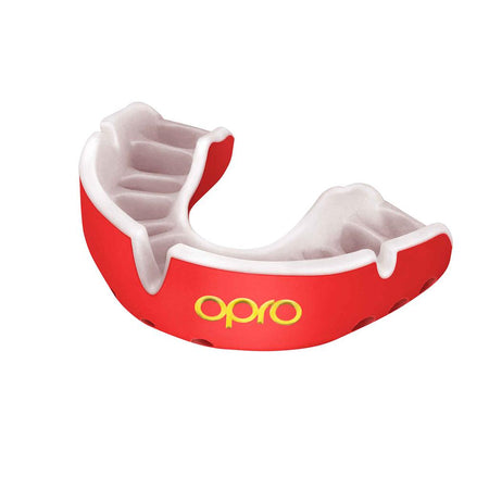 The OPRO Gold Self-Fit Mouthguard by Opro features a red and white design with "opro" in yellow on the front. It fits over upper teeth for protection during sports, making it ideal as a competition level gum shield.