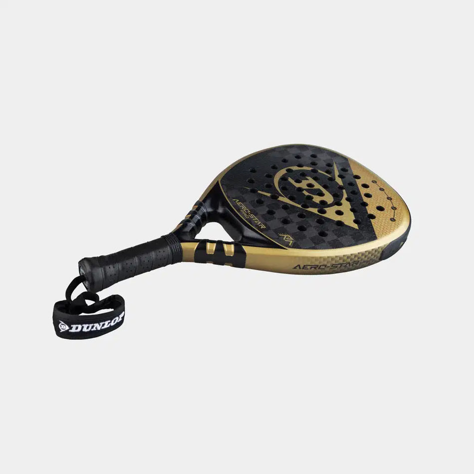 The Dunlop Aerostar Pro Padel Racket by Dunlop features a black and gold design, Power Holes, a perforated surface, 16K Carbon construction, textured grip, and an attached wrist strap—shown on a plain light background.