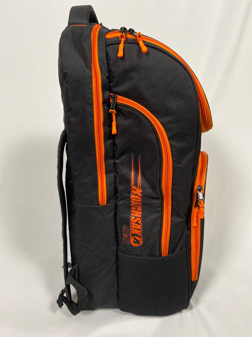 The Katchet KoachSak One2One is a black cricket equipment bag with multiple orange zippers, orange accents, a side pocket, and "MONSTER" printed vertically in orange at the bottom. Designed for one-to-one coaching, it stands upright against a light background.