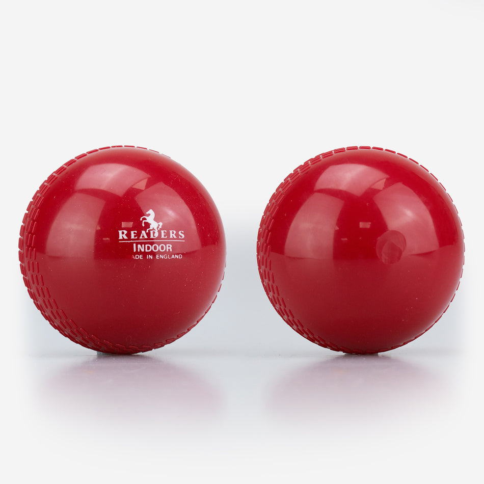 Two shiny red Readers Indoor 4oz Cricket Balls lie side by side on a white surface—one features the Readers logo, while the other highlights its smooth, lightweight plastic design, perfect for indoor training or coaching.