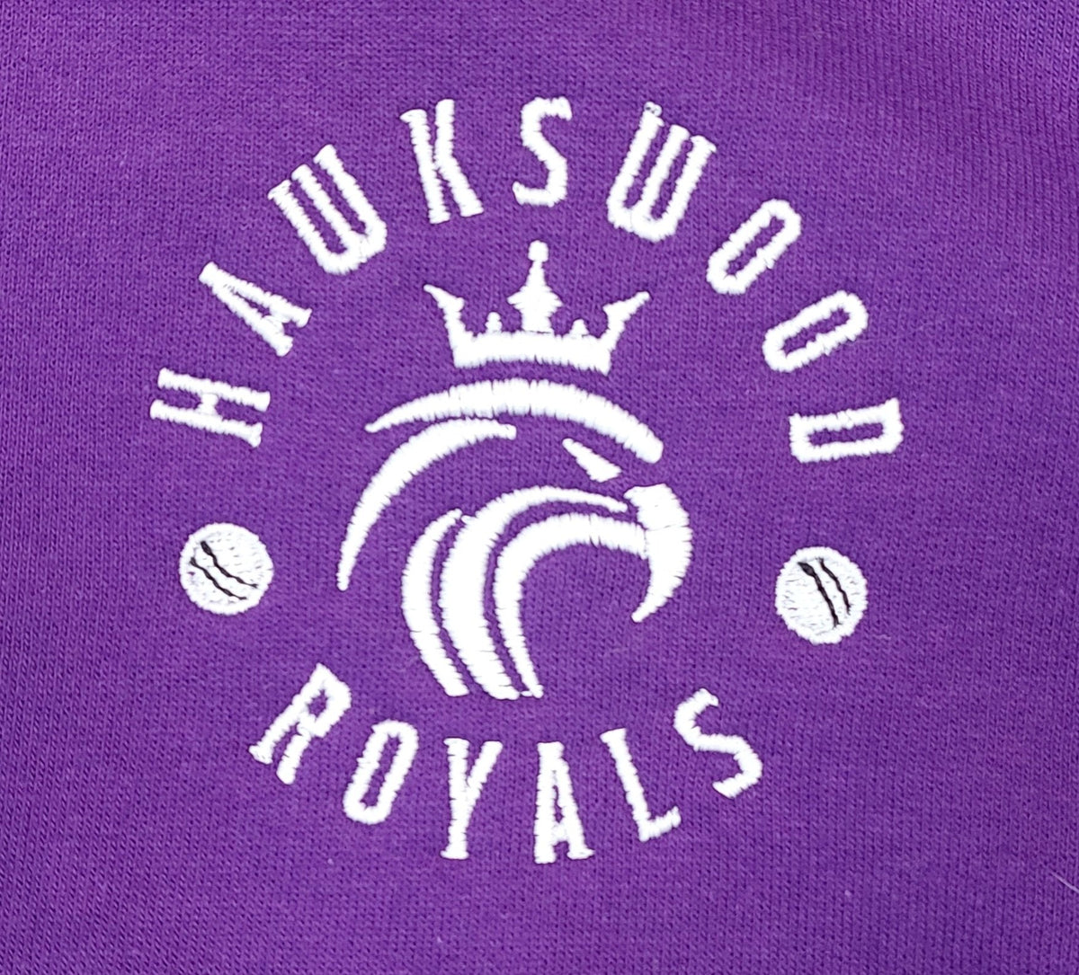 The Hawkeswood Royals Tee Shirt by Martin Berrill Sports features an embroidered white logo with a crowned lion’s head, "HAWKSWOOD ROYALS" text, and baseballs on a purple Neoteric fabric.