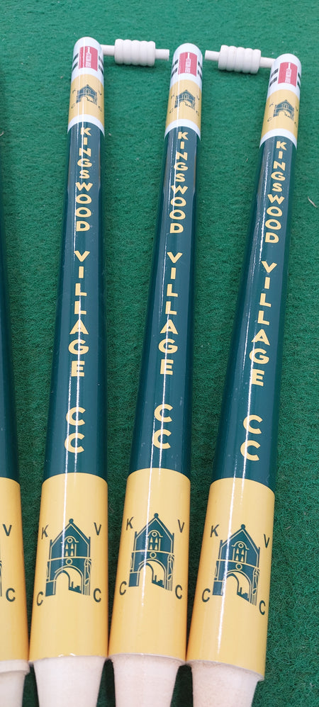 Four Gray Nicolls Custom Printed Club Cricket Stumps featuring the Kingswood Village CCC name and building logo, displayed on a green surface.