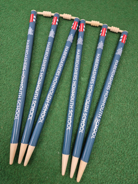Six blue Custom Printed Club Cricket Stumps by Gray Nicolls, arranged fan-like on green grass, resemble personalised cricket stumps. An abacus-style counter is fixed to the top for a unique touch.