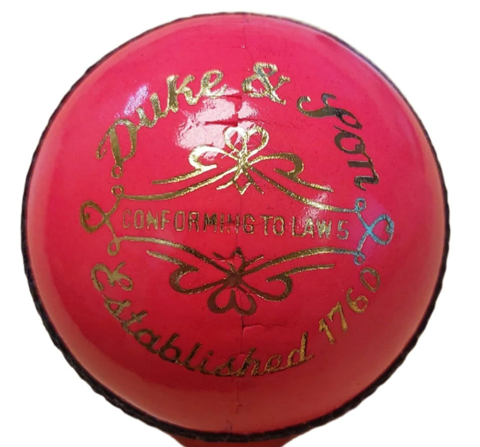 A close-up of the Dukes Special Crown Cricket Ball (Pink, Senior) by Dukes, crafted from English leather with gold "Duke & Son" text, visible stitching, and a shiny finish.