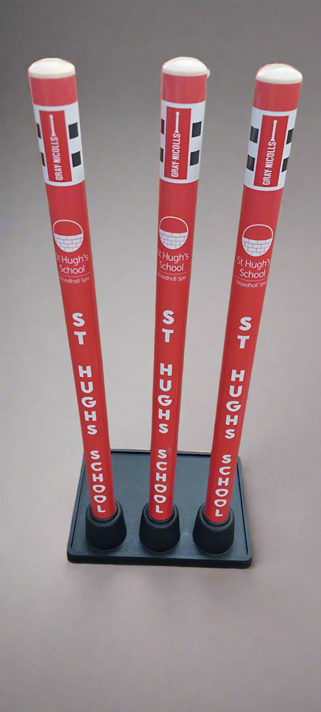 Three red and white Gray Nicolls Custom Printed Match Cricket Stumps with Heavy Rubber Base, featuring checkered patterns, “Drive Slowly,” and St Hugh’s School branding, stand upright on a neutral background.