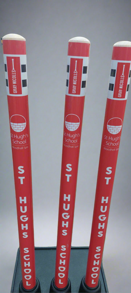 Three red and white Gray Nicolls Custom Printed Match Cricket Stumps with a heavy rubber base, featuring "ST HUGHS SCHOOL Woodhall Spa" text, checkered tops, and "STICK IN HERE" wording on top, shown upright on a plain background.