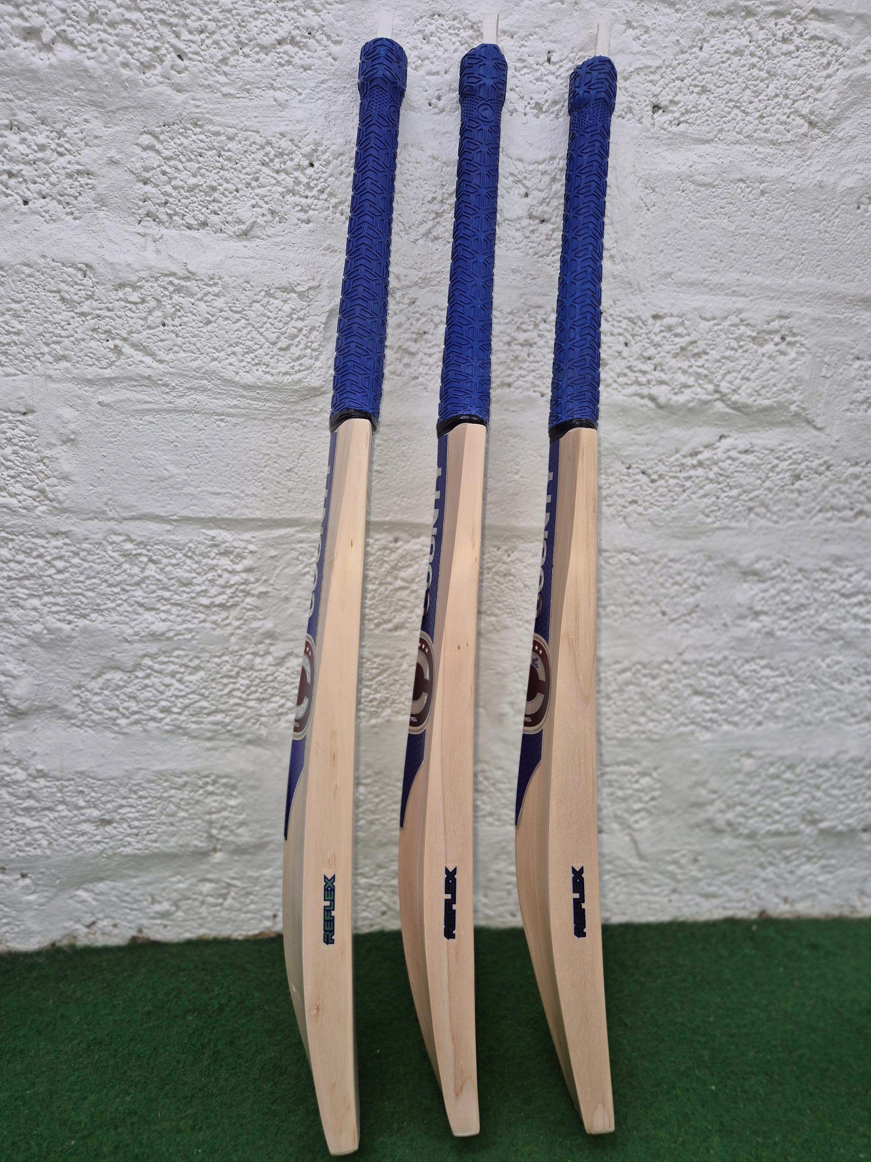 Three Hunts County Reflex Senior Cricket Bats with blue handles stand upright on green turf against a white brick wall—a top pick for senior players by Hunts County.