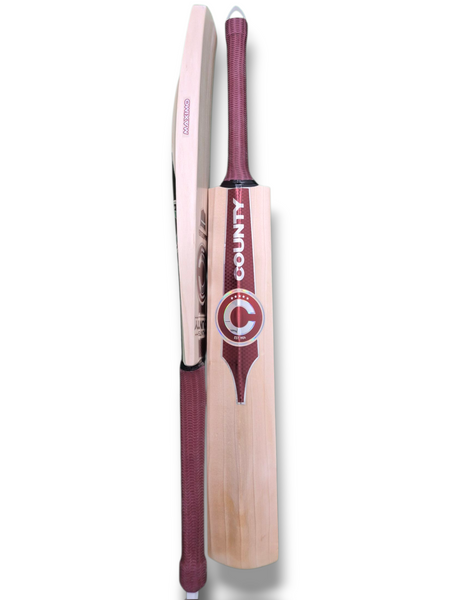 Two Hunts County Maximo Senior Cricket Bats with maroon grips are shown, one displaying the front with the Hunts County brand and logo, the other showing the side profile. Both English Willow cricket bats are placed upright on a white background.
