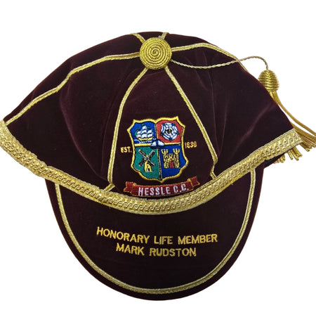 The Custom, Honour & Commemorative Cap by Martin Berrill Sports features maroon velvet with gold trim, tassel, embroidered crest, and can be personalized (e.g., "Honorary Life Member Mark Rudston and Hessle C.C., 1890") with colorful club symbols.