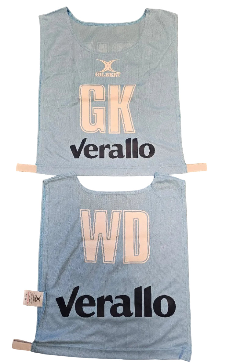 Two light blue Personalised Gilbert Netball Bibs (Single Bibs) with bold cream letters—GK on top, WD below—each featuring "Verallo" and the Gilbert logo above the positions. Ideal for teams seeking quality, custom netball bibs.