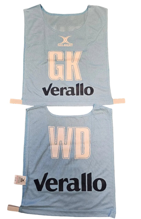 Two light blue Personalised Gilbert Netball Bibs (Single Bibs) with bold cream letters—GK on top, WD below—each featuring "Verallo" and the Gilbert logo above the positions. Ideal for teams seeking quality, custom netball bibs.