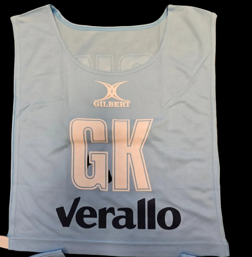 A light blue Personalised Gilbert Netball Bib with the Gilbert logo at the top, large "GK" letters in the center, and "Verallo" in bold black text at the bottom.