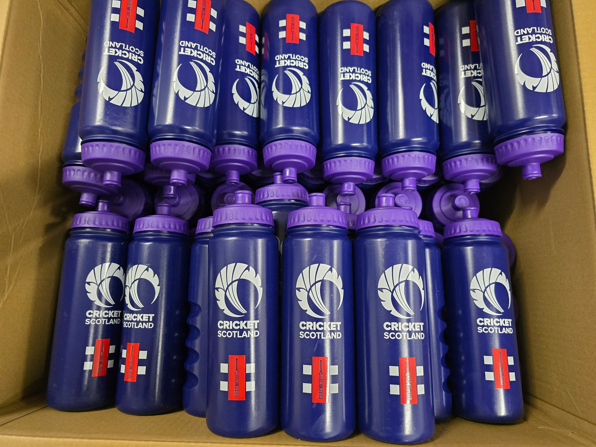 A cardboard box holds Martin Berrill Sports’ Customised Branded Water Bottles, featuring your club or school logo—blue bottles with purple lids, red, white, and blue side designs.