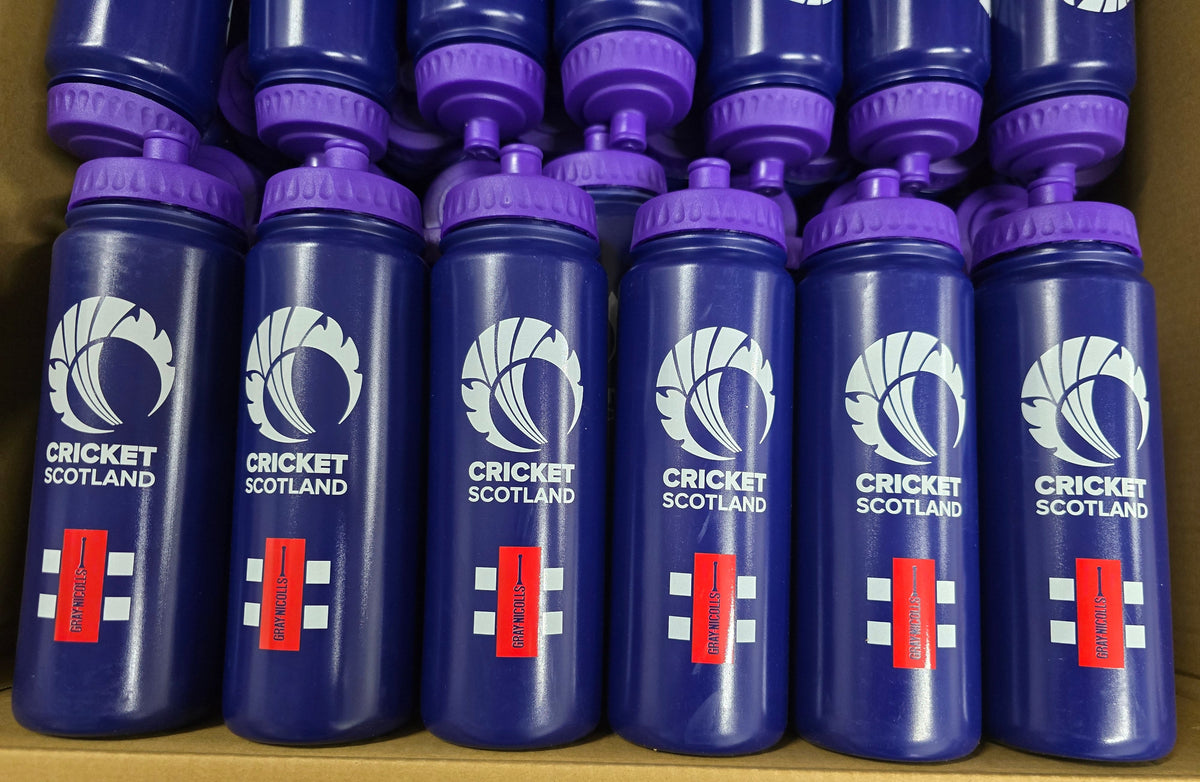 A close-up of multiple blue Martin Berrill Sports Customised Branded Water Bottles, each with a purple lid and club or school logo, neatly arranged in rows inside a cardboard box.