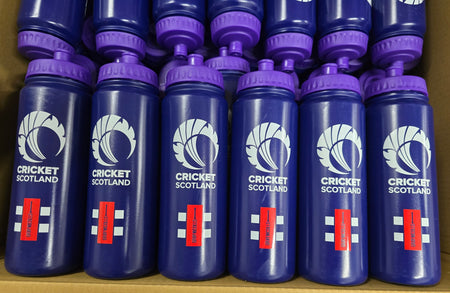 A close-up of multiple blue Martin Berrill Sports Customised Branded Water Bottles, each with a purple lid and club or school logo, neatly arranged in rows inside a cardboard box.