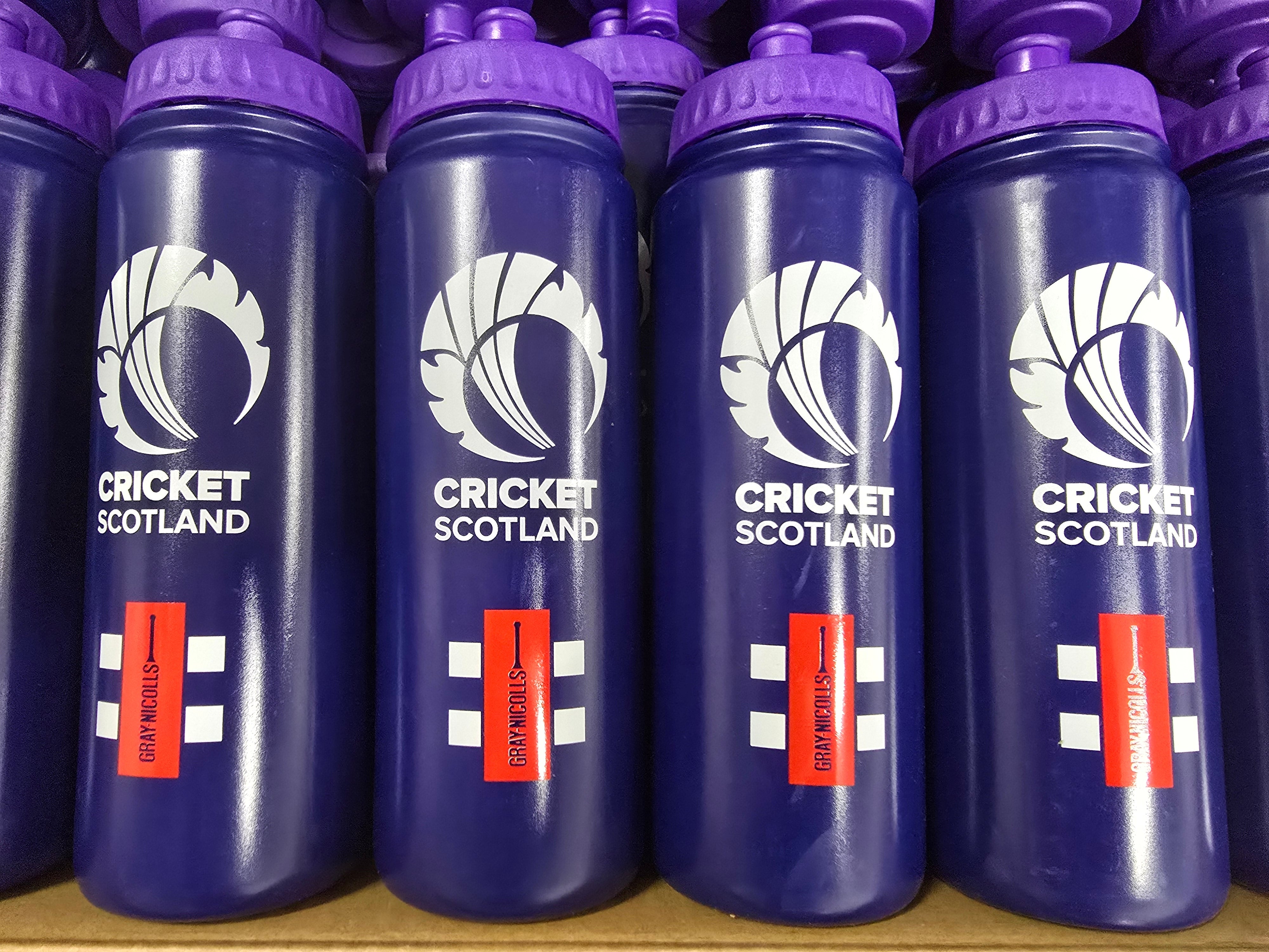 Rows of purple Martin Berrill Sports Customised Branded Water Bottles display a white thistle graphic, your Club or School logo, and red labels boldly stating DRINK ENOUGH in white text.