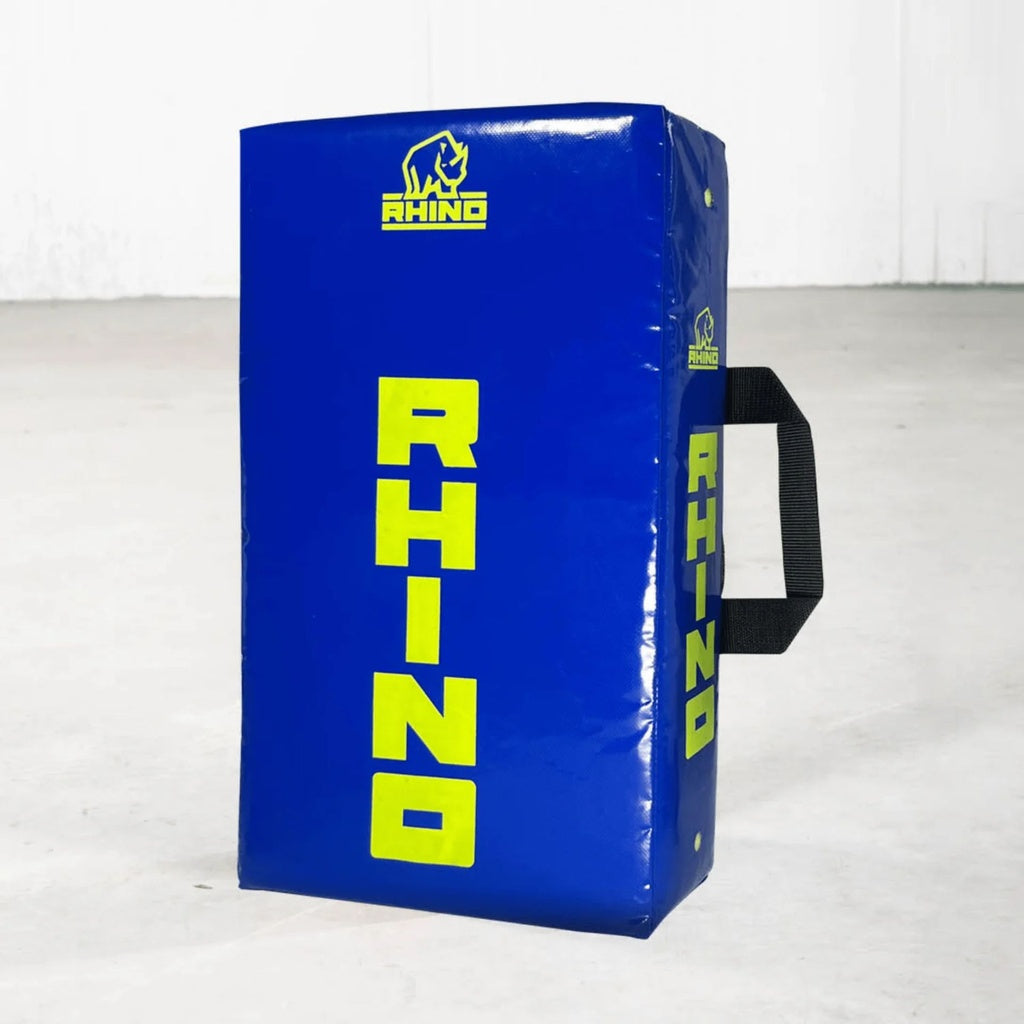 The Rhino Junior Hit Shield by Rhino is a blue rectangular shield for youth rugby training, featuring yellow RHINO text and logo, a black side handle, and displayed on a light floor with a plain white background.
