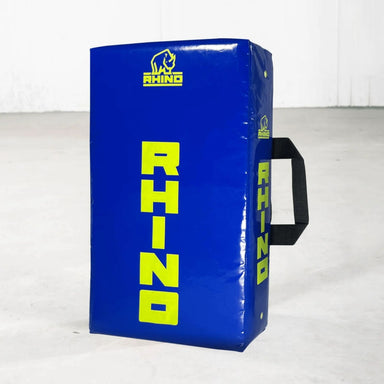 The Rhino Junior Hit Shield by Rhino is a blue rectangular shield for youth rugby training, featuring yellow RHINO text and logo, a black side handle, and displayed on a light floor with a plain white background.