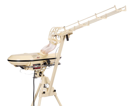 A cream-colored baseball pitching machine with a long arm for launching balls, set on a tripod stand, features an electronic random delivery mode—perfect for solo batting practice. Shown against a white background, it is also compatible with the Bola Automatic 28 ball Feeder Unit by Bola for continuous training sessions.