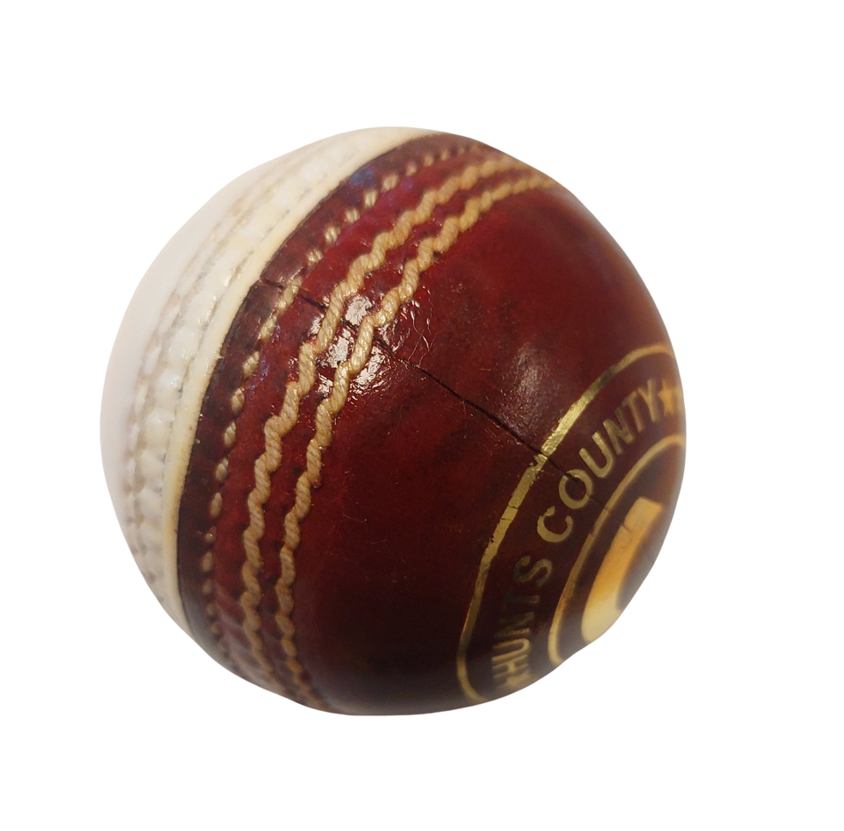 A close-up of the Hunts County Club Training Ball (Red/White) by Hunts County, featuring red leather, white stitching, visible branding, and a surface crack—ideal for swing or spin training—set against a white background.