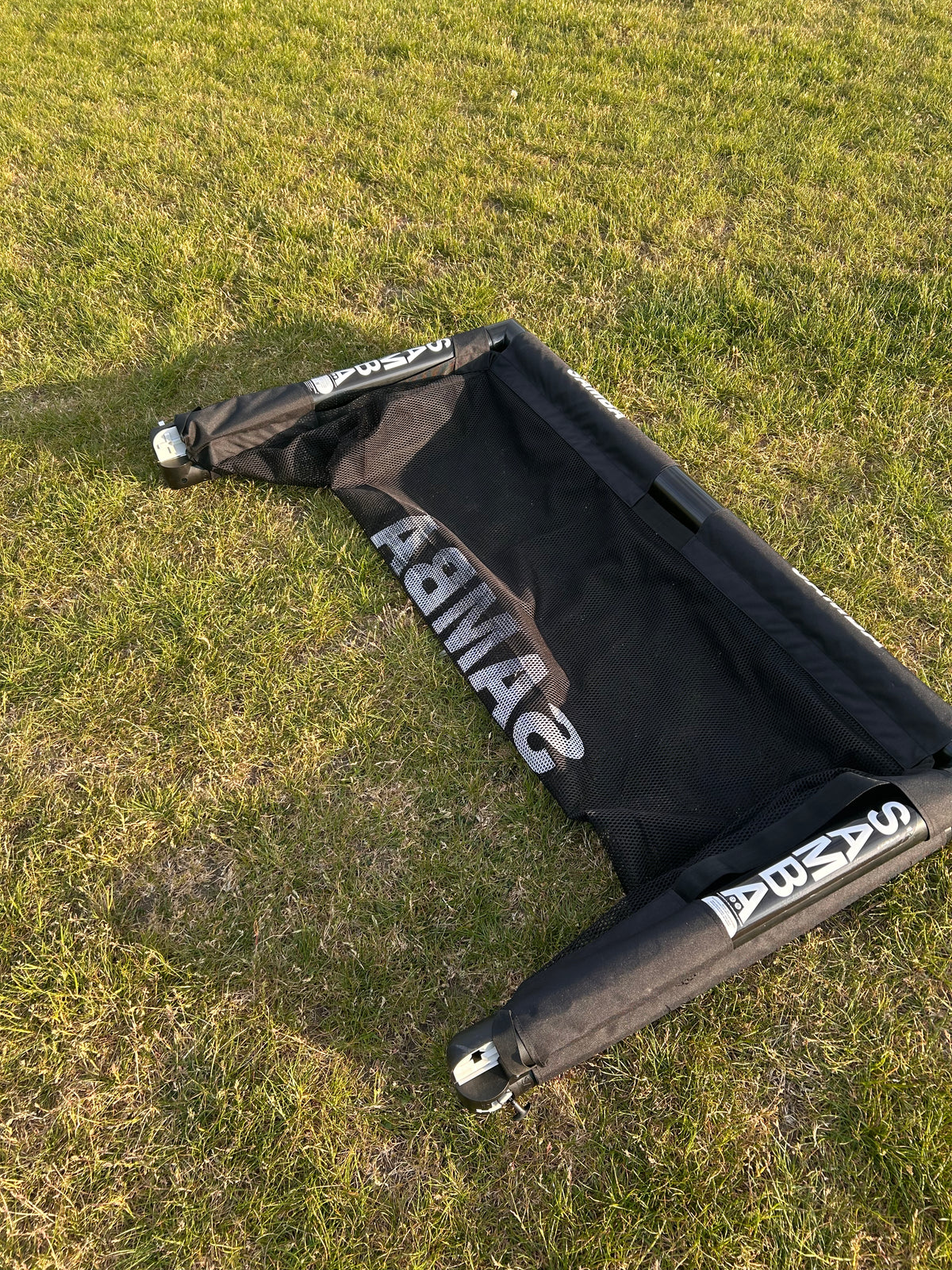A Samba Sports 4ft x 2.5ft Folding 3v3 Goal lies flat and collapsed on the grass, its net and frame visible, showing the portable goal not set up for play.