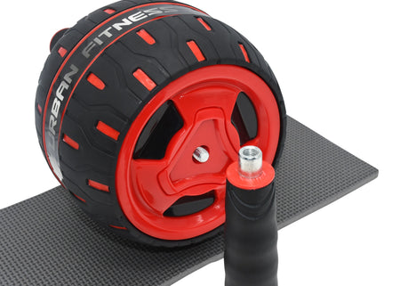 A close-up of the Urban Fitness Rebound Ab Wheel in black and red with branding, on a textured mat; a detachable handle lies in front, making it ideal for building core strength.