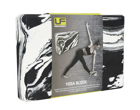 A black/white Urban Fitness Marbled Yoga Block in packaging displays a woman using the firm-density block for support in a yoga pose by a brick wall. The packaging features the Urban Fitness brand name.