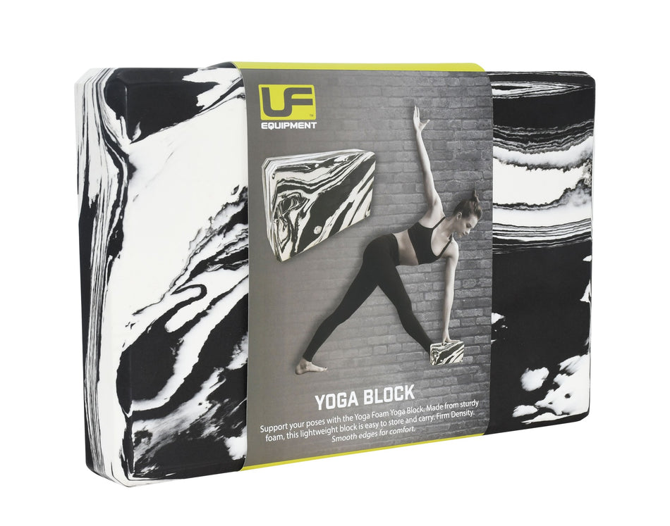 A black/white Urban Fitness Marbled Yoga Block in packaging displays a woman using the firm-density block for support in a yoga pose by a brick wall. The packaging features the Urban Fitness brand name.