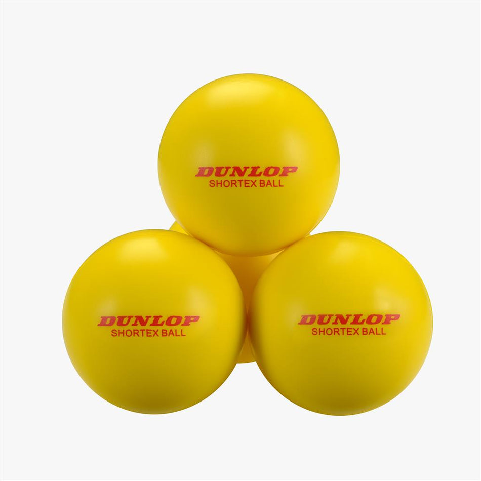 A set of Dunlop Shortex Foam Tennis Balls (12 Pack) by Dunlop are shown stacked on a white background, each bright yellow ball displaying the red Dunlop Shortex Ball logo—ideal for beginner kids' tennis.