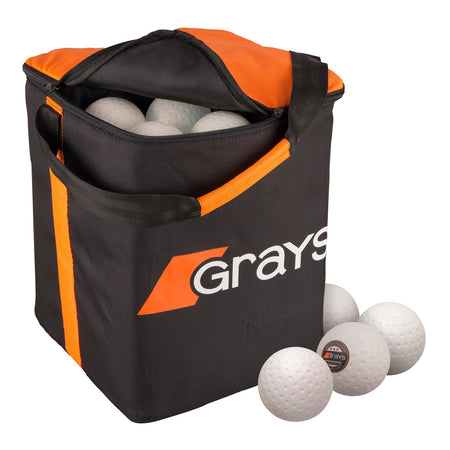 The Grays Hockey Ball Bag by Grays, shown in black and orange with a sturdy handle, is filled with white field hockey balls, with some balls also displayed outside the bag.