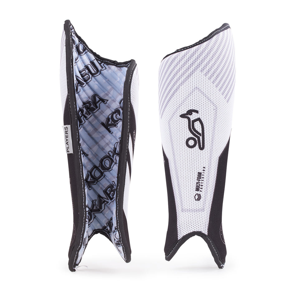 Two Kookaburra Players Shinguards are shown—one displays the front with a wave design and logo, while the other reveals the patterned foam backing and elastic straps.