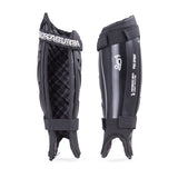 Pair of black Kookaburra Pro Spirit Shinguards: one side shows padded foam backing, the other reveals a hard shell with white logo. Both include ankle straps, foot loops, and reinforced spine for extra support.