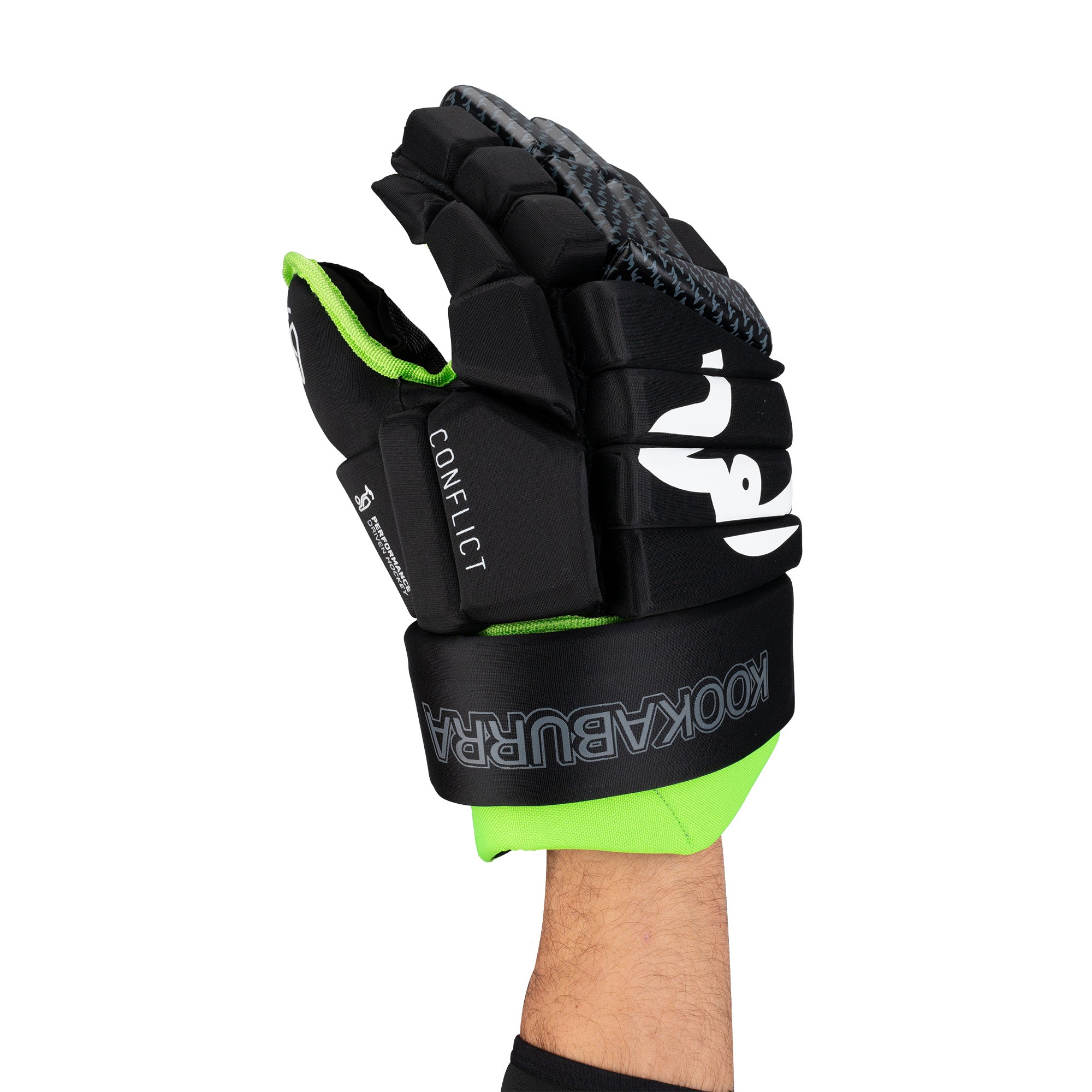 A hand is raised against a white background wearing the Kookaburra Pro Conflict Hockey Glove, featuring black and green colors with high-density foam padding and the Kookaburra brand name printed on the wrist strap.