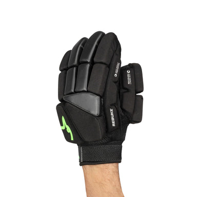 A person wearing a Kookaburra Rebuke Hockey Glove—black high density foam with protective segments and a green Kookaburra logo—photographed against a white background.