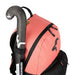 A close-up of the Kookaburra Flow Rucksack 2026 in pink, featuring black zippers, a black-and-white Kookaburra logo, adjustable shoulder straps, and holding a black field hockey stick with white markings in its external side pocket.
