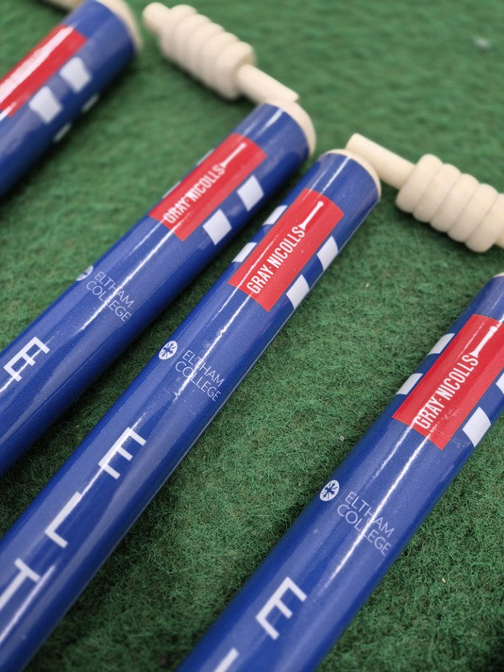 Four blue Custom Printed Club Cricket Stumps with white handles, branded by Gray Nicolls, are laid on green artificial turf. The stumps display crisp logos in white and red.
